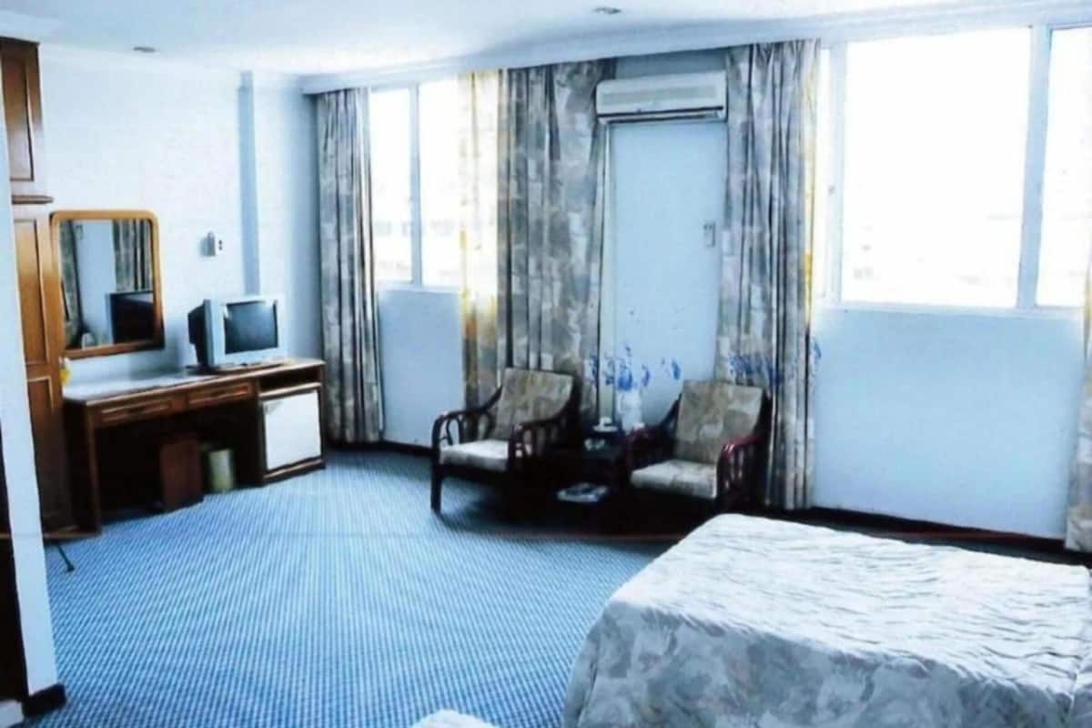 A hotel room with a bed, a desk with a computer, two armchairs, and a large window with curtains.