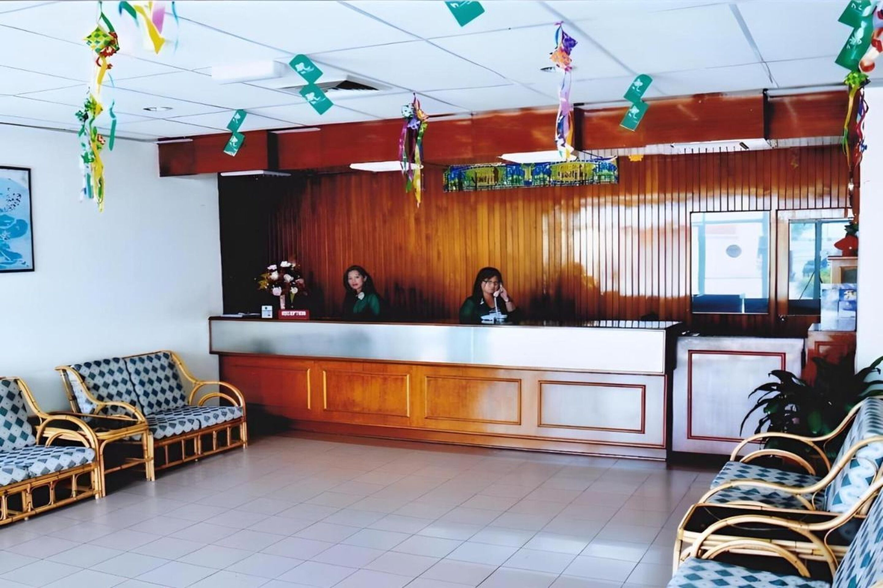 A reception area with a wooden reception desk, two receptionists, and wicker chairs.