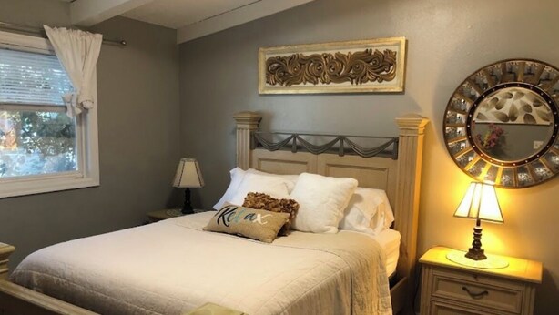 A bedroom with a bed, nightstands, a lamp, a decorative mirror, and a window with curtains. - Turnagain inn  (Anchorage)