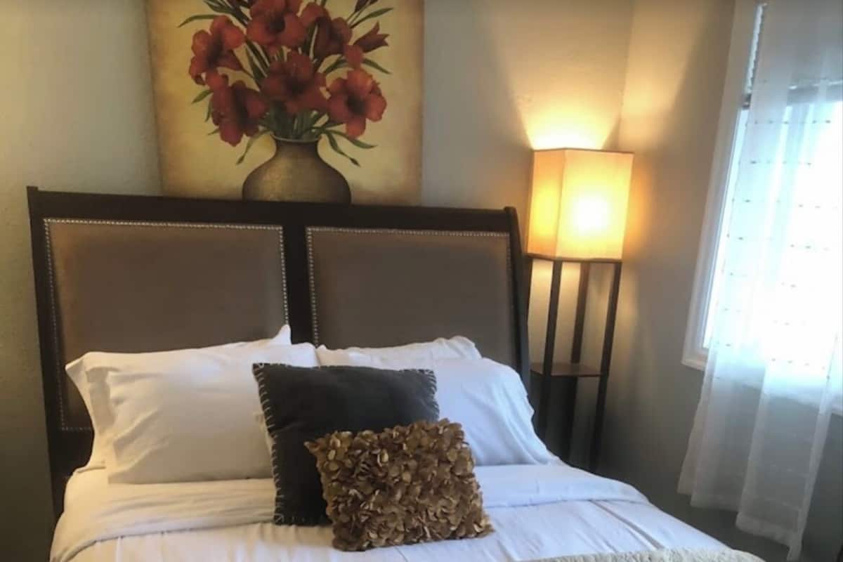 A neatly made bed with a patterned bedspread, a dark pillow, and a decorative pillow.