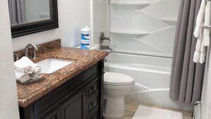 A bathroom with a granite countertop sink, dark cabinetry, a white toilet, a bathtub, and a shower curtain. - Turnagain inn  (Anchorage)