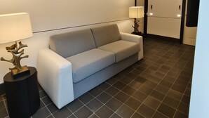 A modern hotel room with a white sofa, a black floor lamp, and a ceiling light fixture. - Altoledo Rooms and Suite (Naples)