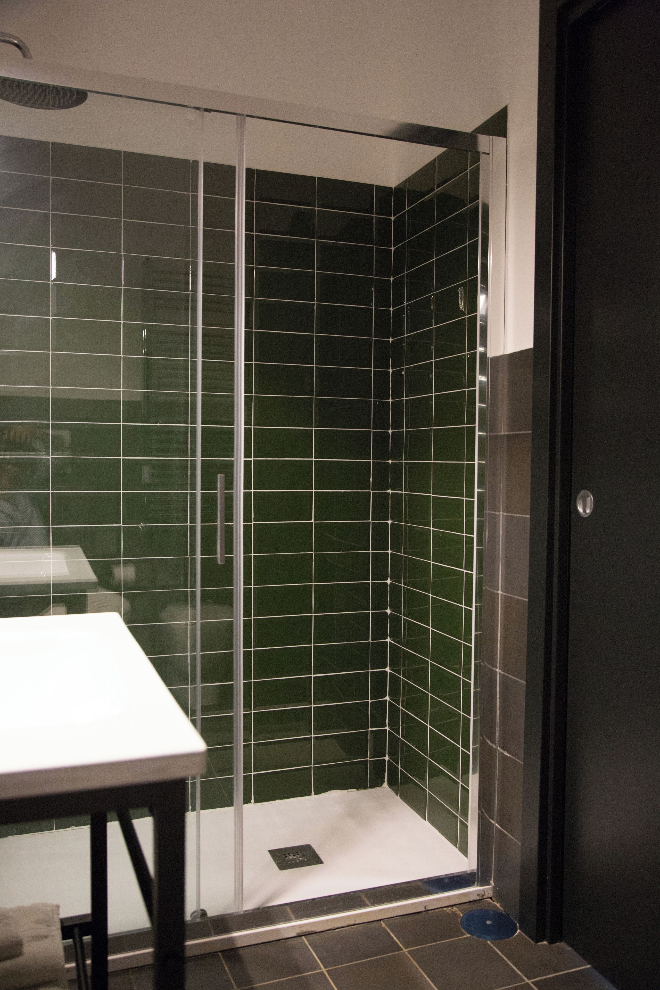 A shower with green tiles and a white door.