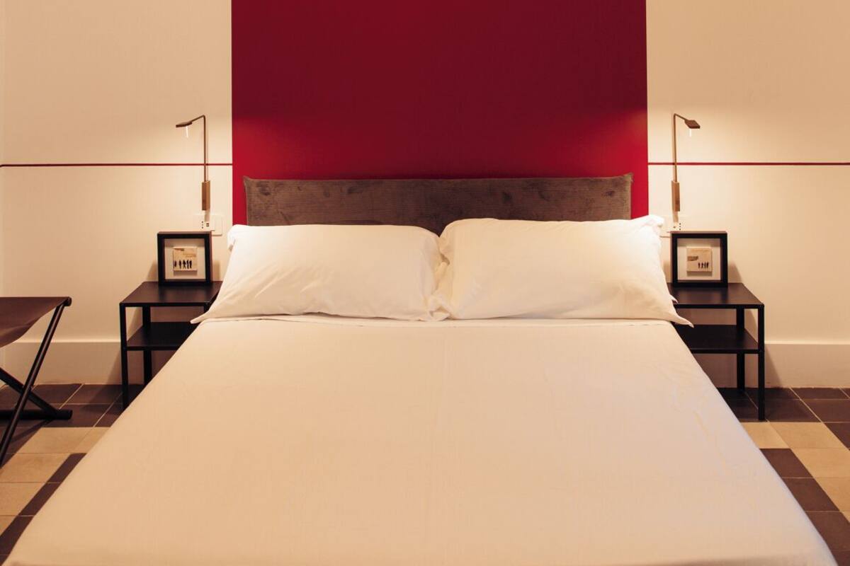 A modern bedroom with a large bed, two bedside tables, and a red accent wall.