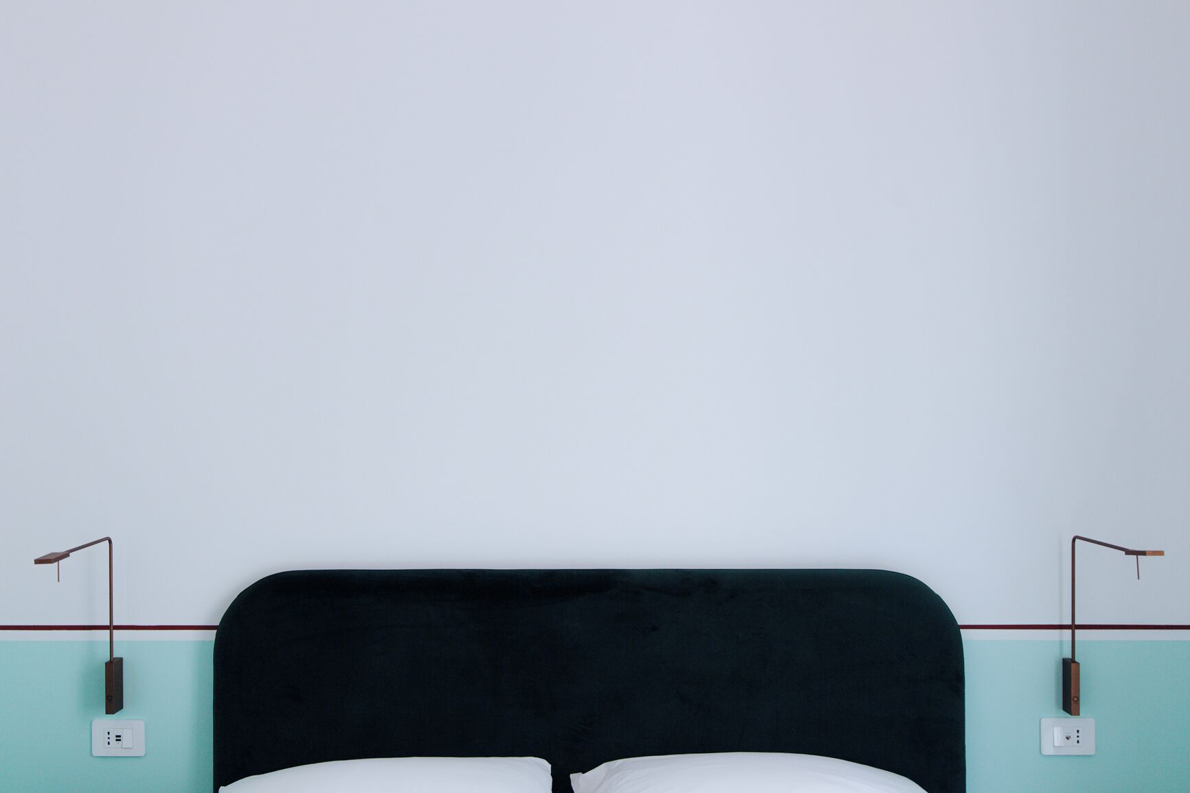 A bed with a black headboard, white pillows, and a teal wall with two bedside tables and lamps.