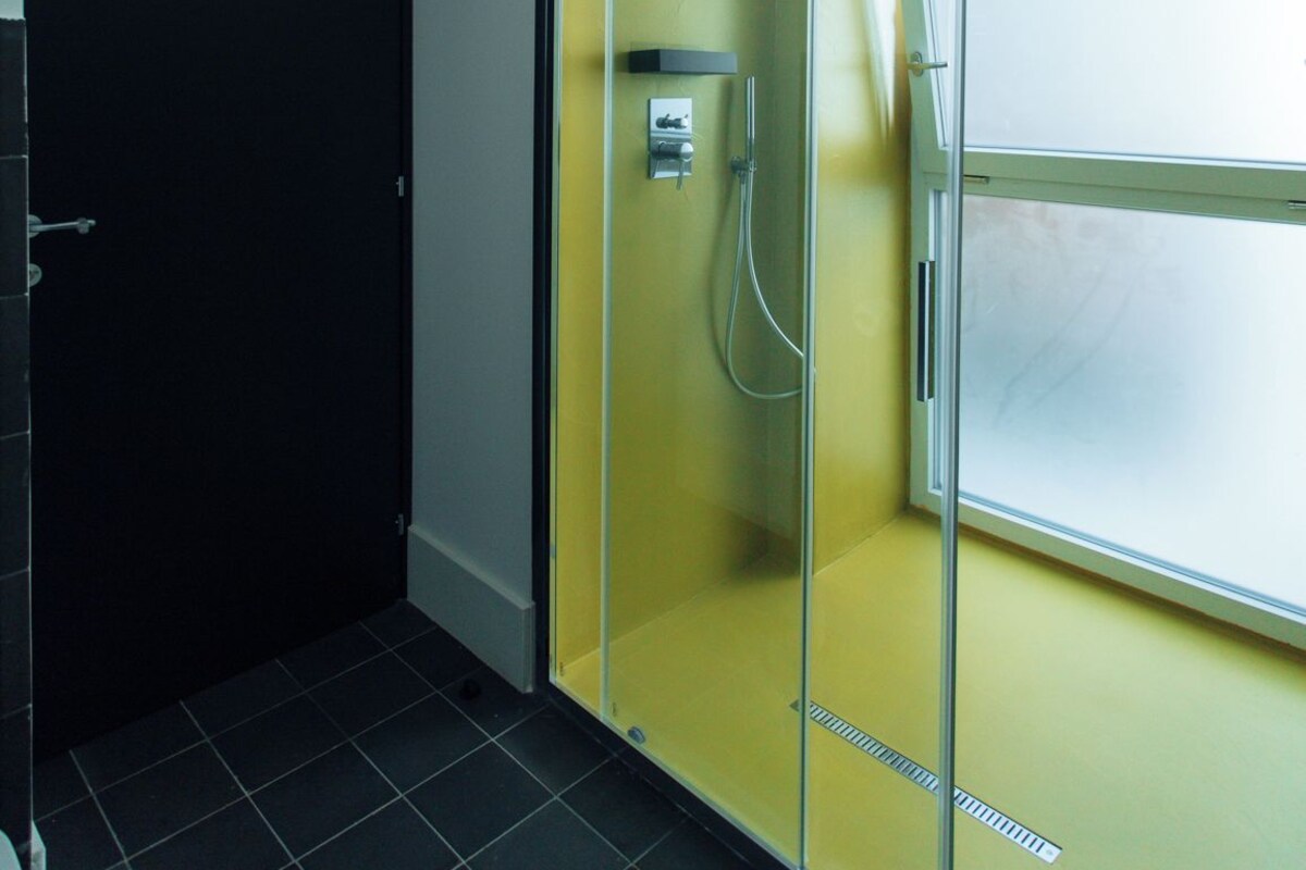 A bathroom with a glass-enclosed shower, a black door, and a yellow wall.