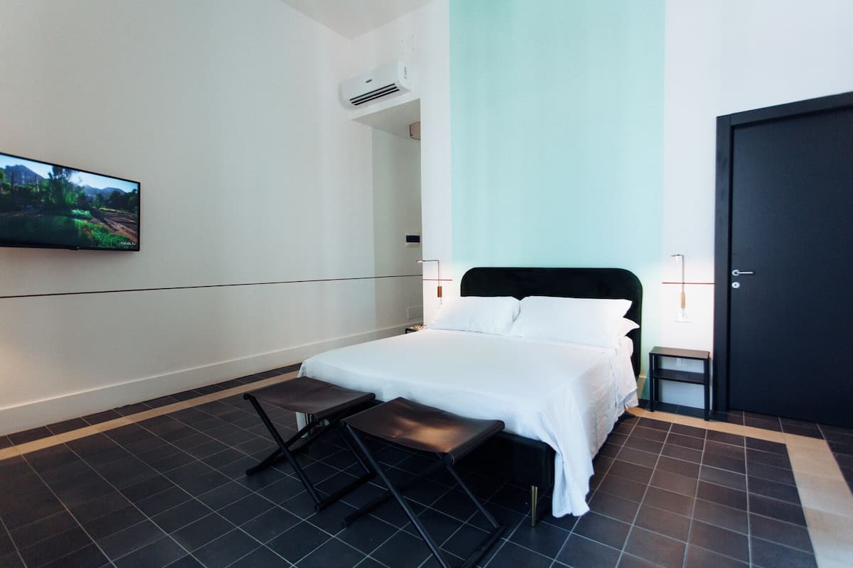 A hotel room with a bed, a TV mounted on the wall, a small bedside table, and a door.