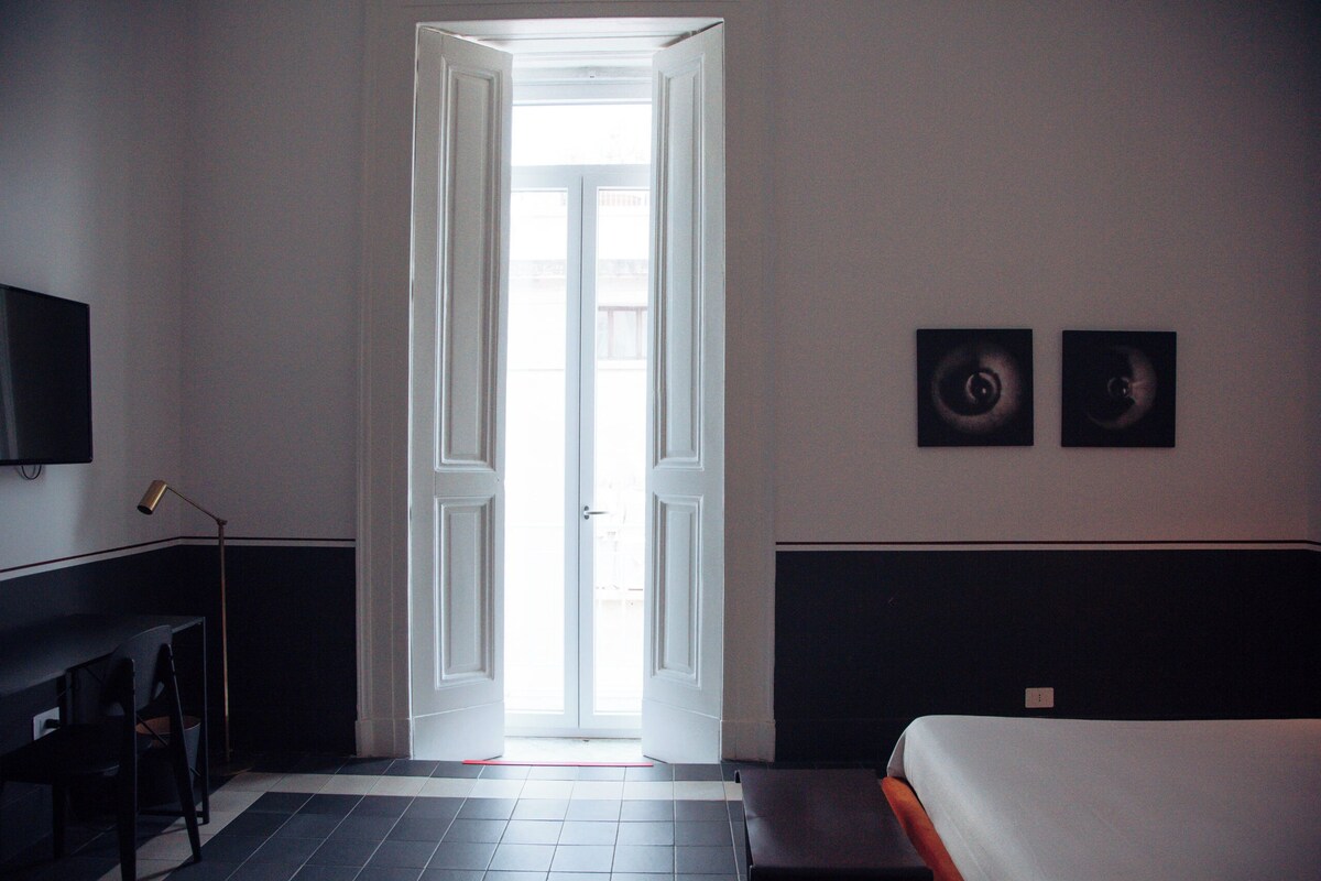 A hotel room with a bed, a desk, a chair, and a television on the wall.