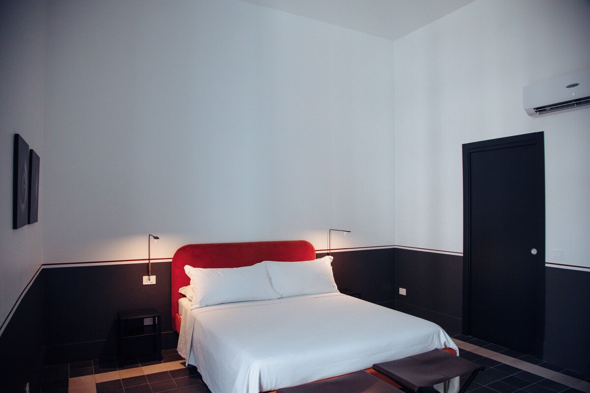 A hotel room with a bed, bedside tables, a wall-mounted air conditioner, and a door.