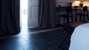 A hotel room with a bed, a desk with chairs, a lamp, and a door leading outside. - Altoledo Rooms and Suite (Naples)