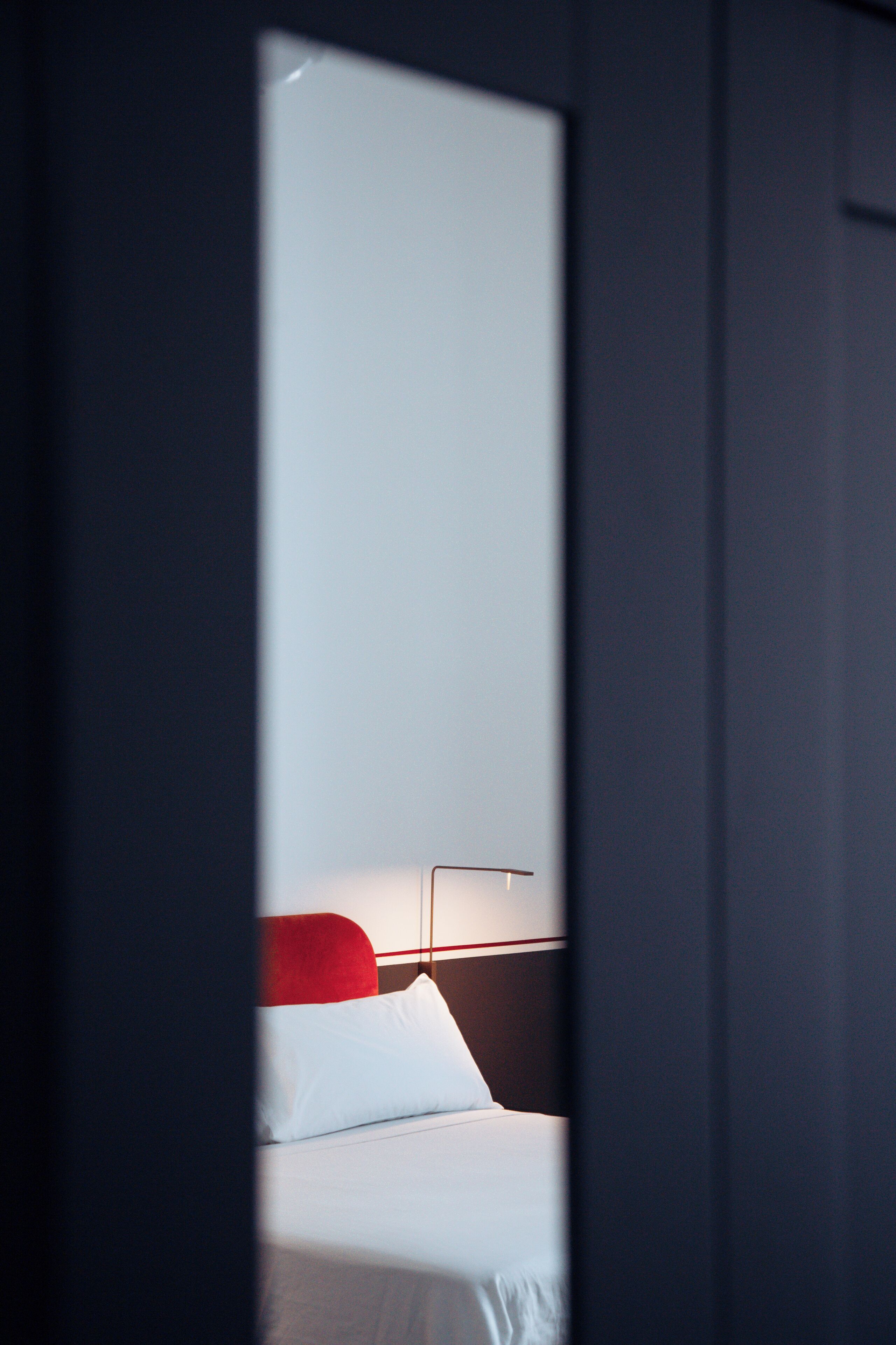 Une chambre d’hôtel avec un lit, une tête de lit rouge et une table de chevet avec une lampe.