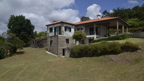 A two-story house with a stone foundation, a red-tiled roof, and a covered porch. - Quinta de Maiores (Ovil)