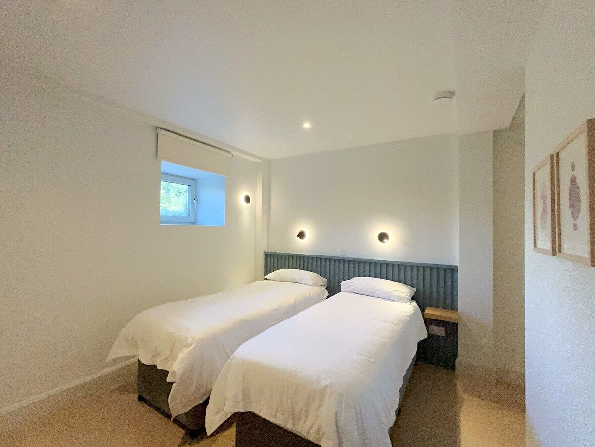 A room with two single beds, a window, and a wall-mounted light fixture.