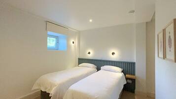 A room with two single beds, a window, and a wall-mounted light fixture.