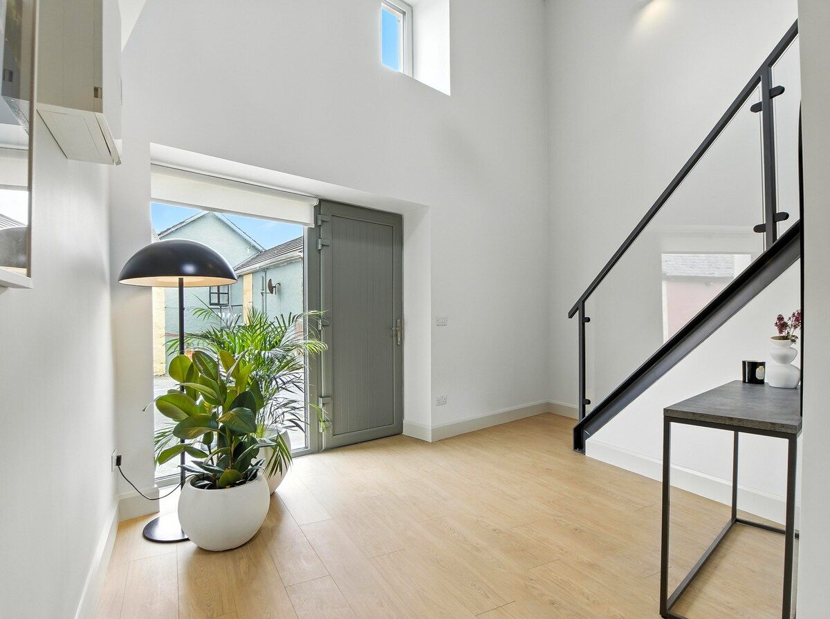 A modern interior with a staircase, a potted plant, and a view through a door.