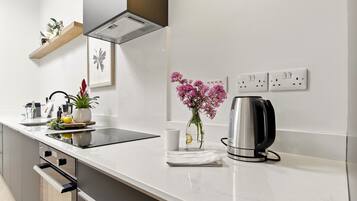 Una cocina moderna con encimera blanca, electrodomésticos de acero inoxidable, una cafetera y un florero con flores.