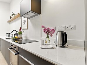 Una cuina moderna amb taulell blanc, electrodomèstics d'acer inoxidable, una cafetera i un ram de flors.