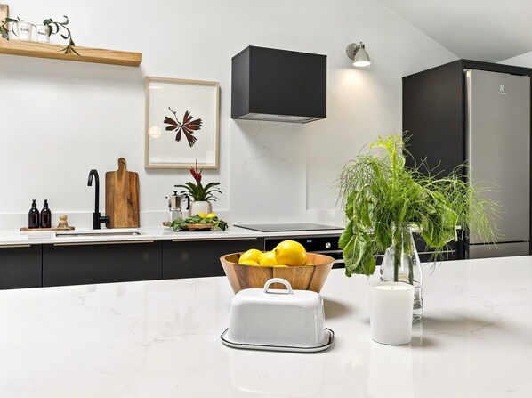 A modern kitchen with a marble countertop, a wooden bowl of lemons, a white toaster, and a potted plant.