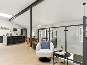 Un interior modern amb una butaca blanca, una zona de menjador i una cuina.