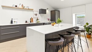 A modern kitchen with a large island, bar stools, and a view of the outdoors. - The Warehouse, Clifden Modern and elegant (Clifden)