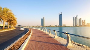 A waterfront promenade with a paved walkway, palm trees, and modern buildings in the background. - OYO 1558 Belvilla Top Stars Hotel Near Gold Souk (Abu Dhabi)