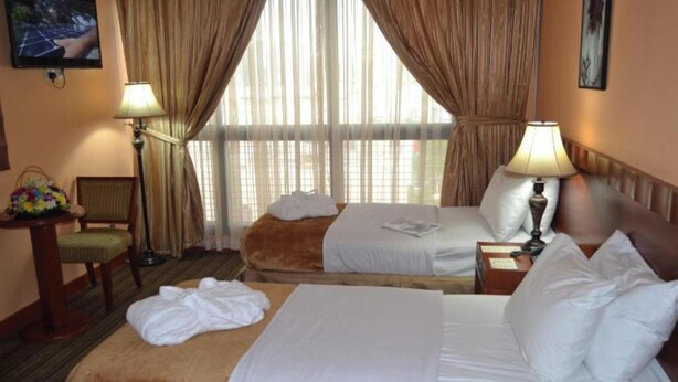 A hotel room with two beds, a chair, a table with a lamp, and a window with curtains. - OYO 1558 Belvilla Top Stars Hotel Near Gold Souk (Abu Dhabi)