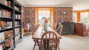 Un comedor con una larga mesa de madera, sillas y una estantería llena de libros.