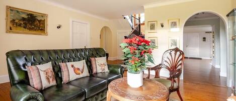 A living room with a green leather sofa, a wooden coffee table, and a floral centerpiece.