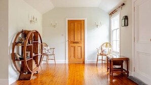 Una habitación con suelo de madera, una puerta de madera, una silla, una mesa y un ventanal con vidrieras.