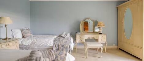 A bedroom with a bed, a dresser, a vanity with a mirror, and a wardrobe.