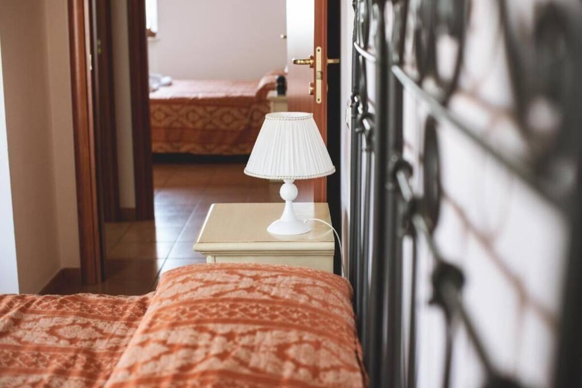 A bedroom with a patterned bedspread, a bedside table with a lamp, and a door leading to another room.