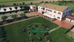 A large, two-story building with a tiled roof, surrounded by well-maintained lawns and a circular garden. - Miraconero (Porto Recanati)