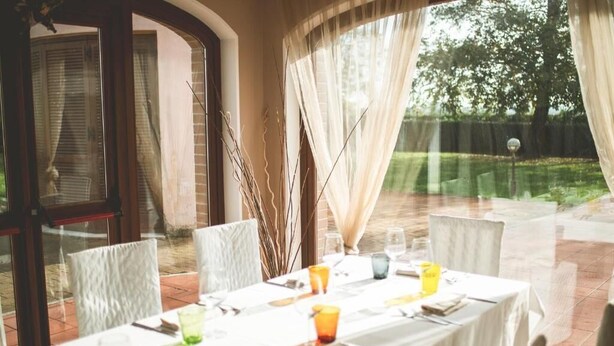 An outdoor dining area with a table set for four, surrounded by chairs, and a view of a garden and trees. - Miraconero (Porto Recanati)