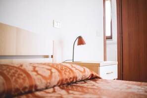 A bedroom with a bed, a nightstand, a lamp, and a window.