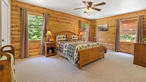 A log cabin bedroom with a wooden bed, a ceiling fan, and large windows with curtains. - Timber Ridge Retreat by Chatuge Home Concierge | Serene Mountain Escape · Stunning Year-Round Views · Gated Community (Hiawassee)