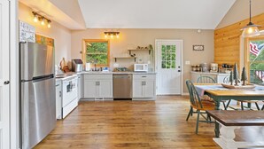 A spacious kitchen with a refrigerator, stove, microwave, and dishwasher. There is a dining area with a table and chairs. - Timber Ridge Retreat by Chatuge Home Concierge | Serene Mountain Escape · Stunning Year-Round Views · Gated Community (Hiawassee)