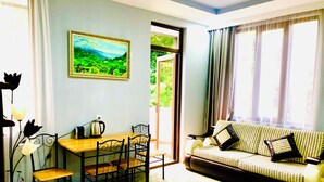 A room with a wooden dining table, four chairs, a sofa with patterned cushions, a painting of a landscape, and a view of greenery through an open door. - Holiday House Green Cape Batumi (Batumi)