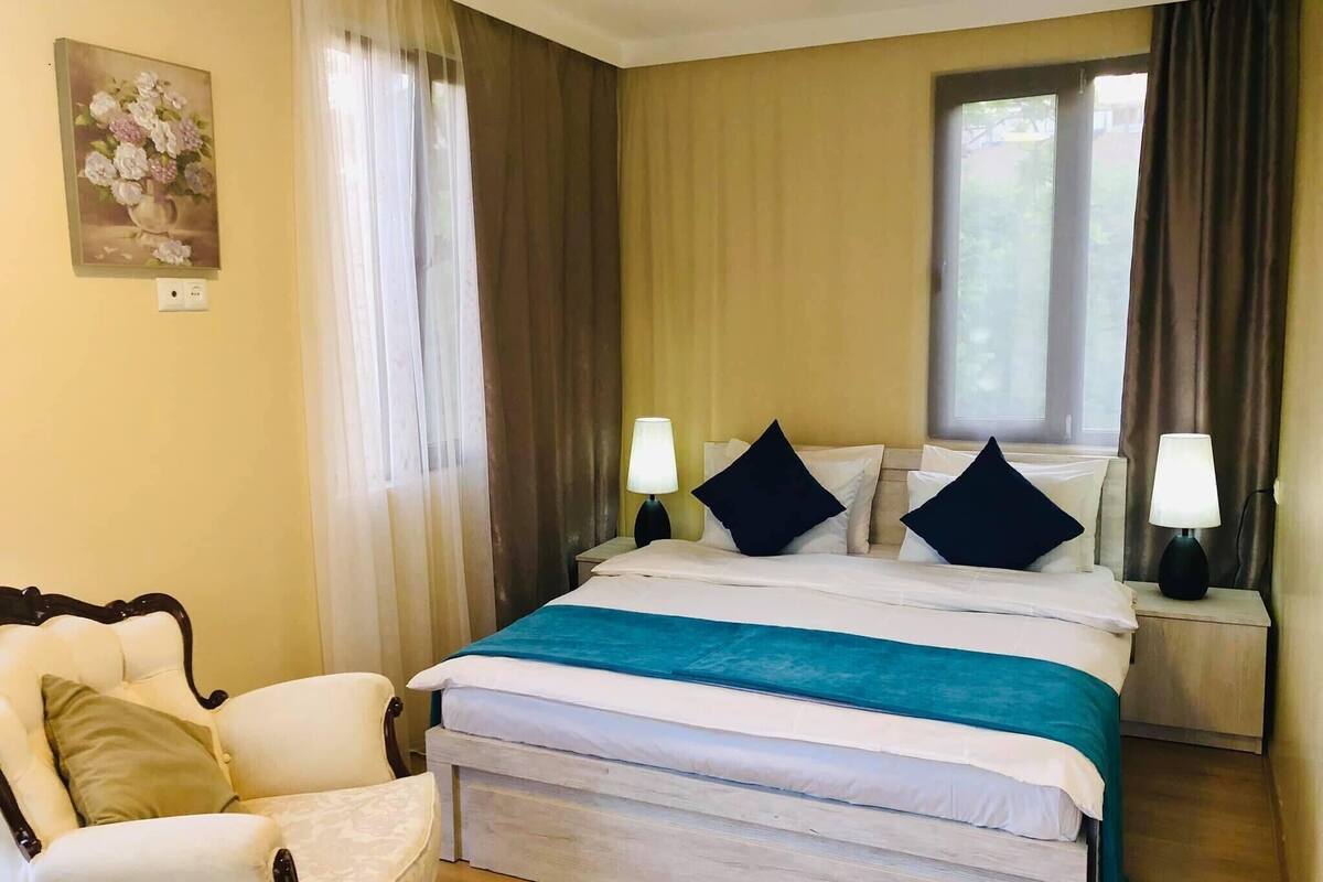 Une chambre d’hôtel avec un lit, deux lampes de chevet, une chaise et un tableau au mur.