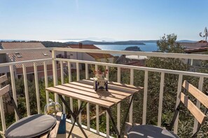 A balcony with a wooden table and chairs, overlooking a body of water and distant mountains.