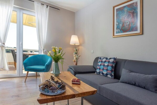 Una sala de estar moderna con un sofá gris, un sillón azul, una mesa de centro de madera y un jarrón con flores.
