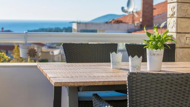 Ein Balkon mit Tisch und Stühlen, einem Blumentopf und Blick auf das Meer und Gebäude.