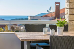 Un balcón con una mesa, sillas, una planta en maceta y vistas al mar y edificios.