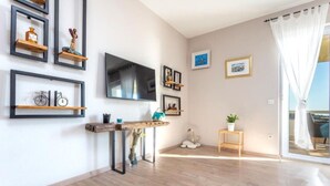 Ein modernes Wohnzimmer mit einem Flachbildfernseher, Holzregalen mit Dekoration, einer rustikalen Holzbank und einem kleinen Tisch mit einer Topfpflanze.