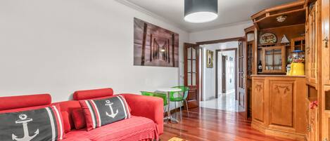 Una sala de estar con sofá rojo, armarios de madera y una silla verde.