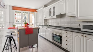 A modern kitchen with white cabinetry, a central island with stools, a stove, and a microwave. - Apartment 'O Faro Apartamentos' with Sea View, Balcony and Air Conditioning (Ribadeo)