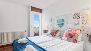 A double bed with a blue and white bedspread, two rolled towels, and a wall with various art pieces. - Apartment 'O Faro Apartamentos' with Sea View, Balcony and Air Conditioning (Ribadeo)