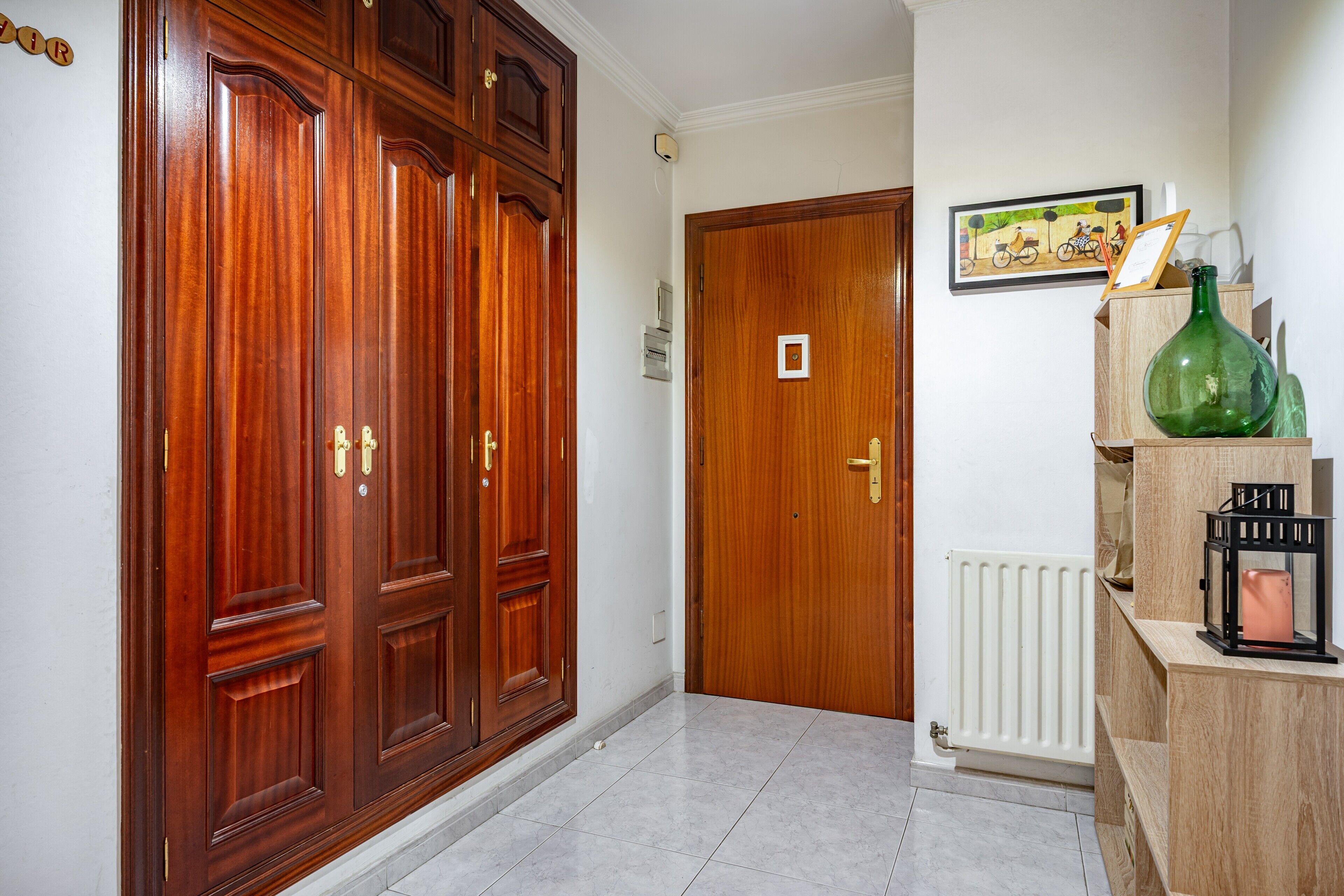 Un couloir avec des portes en bois, un radiateur et un tableau encadré accroché au mur.