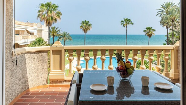 Un balcone con un tavolo in vetro, una ciotola di frutta e vista sull'oceano e sulle palme.