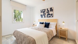 Camera da letto con un letto, comodini, una ventola a soffitto, opere d'arte e una finestra vista alberi.