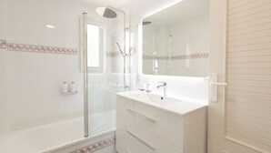 Un bagno moderno con doccia vetrata, un mobile lavabo bianco con specchio e pavimento piastrellato.